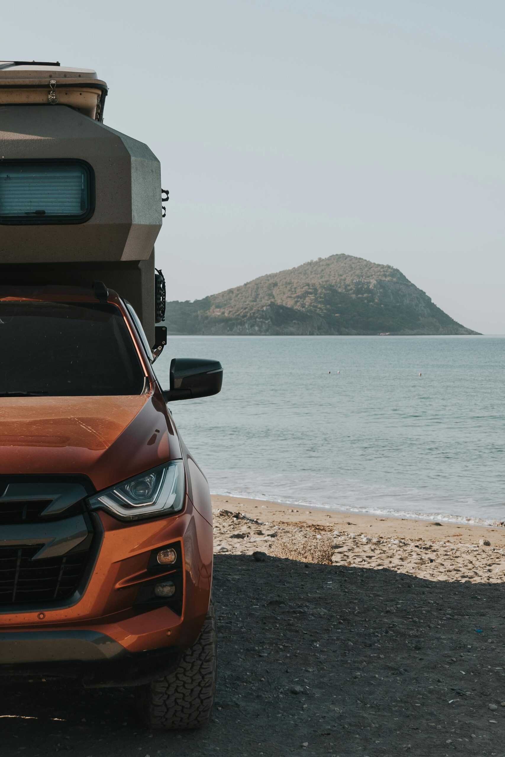 A camper van parked by a tranquil beach with a mountain view, ideal for summer travel.